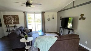 Uma sala de estar com sofá, mesa de centro, televisão em móvel e ventoinha no teto.
