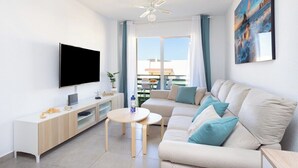 A modern living room with a flat-screen TV, a sofa, a coffee table, and a ceiling fan. - Home2Book Comfy Seaside Apartment Cristimar, Pool (Los Cristianos)