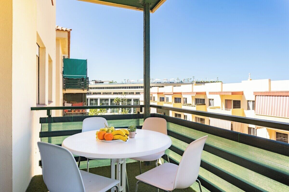 Un balcon avec une table ronde et quatre chaises, une petite plante en pot et un saladier de fruits.
