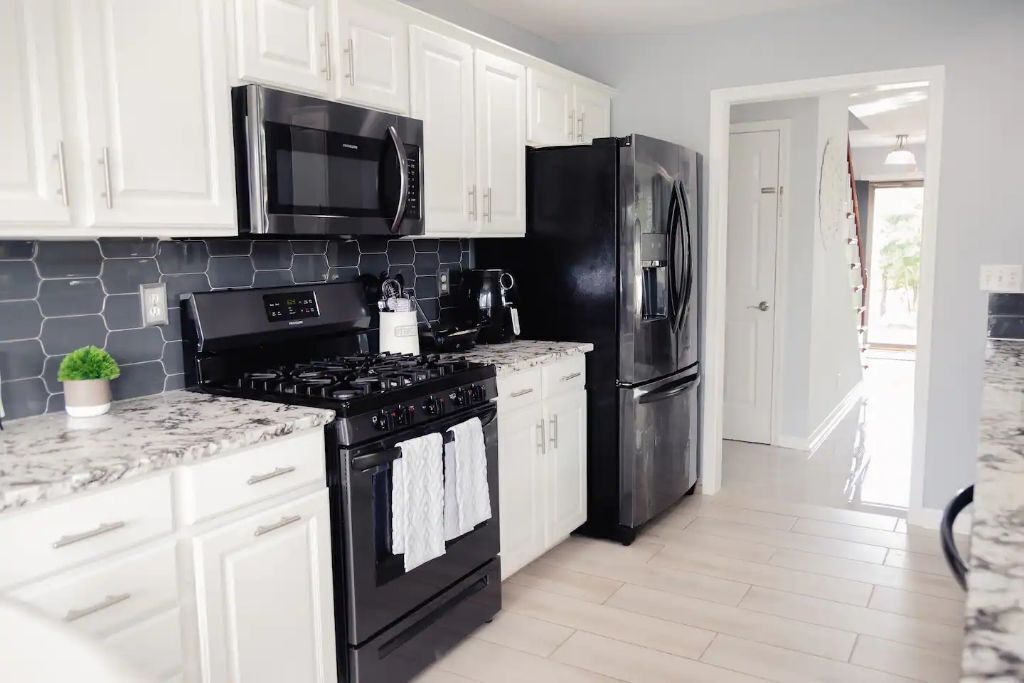 A modern kitchen with white cabinets, a black stove, a stainless steel refrigerator, and a microwave.