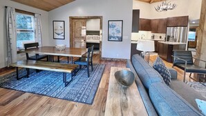 Amplia sala de estar con una mesa de comedor de madera, un sofá y una cocina al fondo.