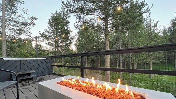 An outdoor deck with a rectangular fire feature surrounded by rocks, a metal bench, and a wooden railing. - Echo Summit Cabin: Hot Tub, 1mi to Sierra at Tahoe (Twin Bridges)