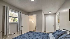 A bedroom with a bed, a window with curtains, a door leading to a bathroom, and a mirror on the wall. - Near Mines & Meadows: Spacious Home w/ Game Room (Beaver Falls)