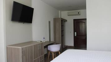 Una habitación de hotel con una cama, un escritorio con una silla, un armario, un televisor y aire acondicionado.
