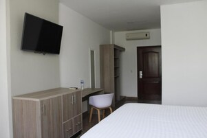 Una habitación de hotel con una cama, un escritorio con una silla, un armario, un televisor y aire acondicionado.