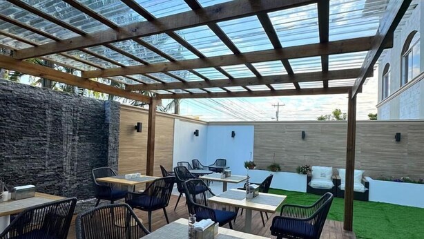 Une terrasse extérieure avec des tables et des chaises en bois, un mur en pierre et une structure de toit en verre.