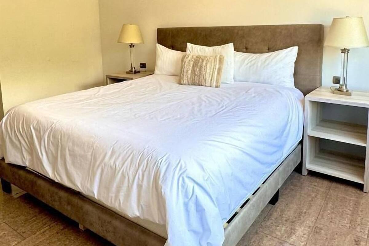 A neatly made bed with white linens, a headboard, and two bedside tables with lamps.