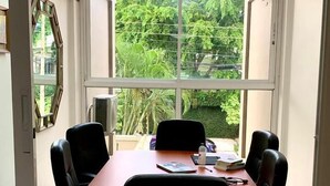 Une salle de conférence avec une longue table, des chaises de bureau noires et une vue sur la verdure à l’extérieur.