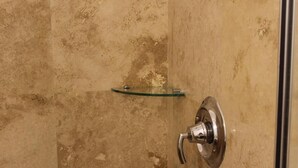Une douche avec une étagère en verre et un robinet chromé.