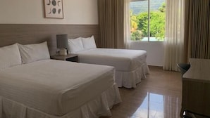 Une chambre d’hôtel avec deux lits, une table de chevet avec une lampe, un tableau encadré au mur et une grande fenêtre avec des rideaux.