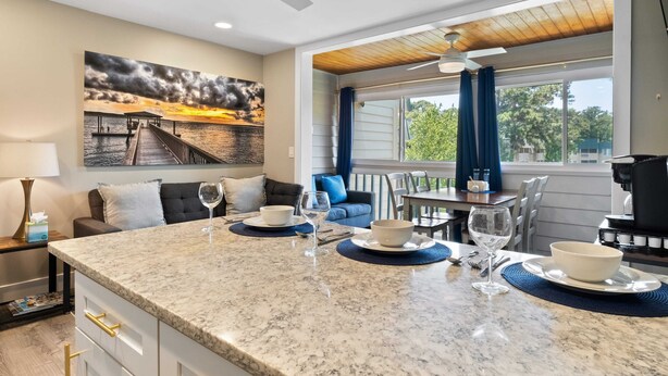 A modern kitchen with a granite countertop, dining area, and a large window with curtains.
