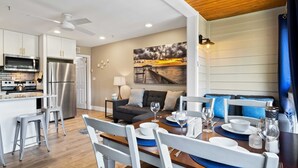 A modern kitchen with white cabinets, stainless steel appliances, and a dining area with a wooden table and white chairs.