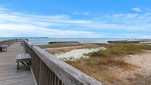 A wooden boardwalk leading to a beach with a clear view of the ocean and distant land.