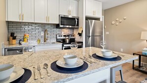 A modern kitchen with white cabinets, a stainless steel refrigerator, a microwave, and a granite countertop.