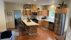 A modern kitchen with wooden cabinets, stainless steel appliances, and a central island with bar stools. - Charming Gig Harbor Getaway (Gig Harbor)