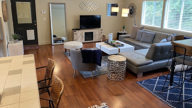 A modern living room with a sofa, coffee table, ottoman, and a TV. - Charming Gig Harbor Getaway (Gig Harbor)