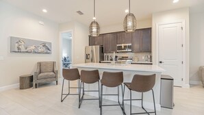 A modern kitchen with a central island, bar stools, dark wooden cabinets, stainless steel appliances, and pendant lighting. - The Blue Heron | Heated Pool and Outdoor Grill | Near Beach (Naples)
