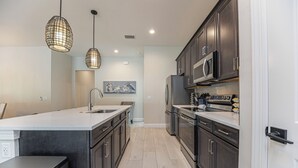 A modern kitchen with dark cabinetry, a large island, stainless steel appliances, and pendant lighting. - The Blue Heron | Heated Pool and Outdoor Grill | Near Beach (Naples)