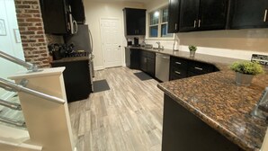 Una cocina moderna con armarios oscuros, encimera de granito y pared decorativa de ladrillo.