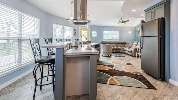 Una cocina moderna con una isla central, una zona de comedor con sillas, un sofá y un refrigerador.