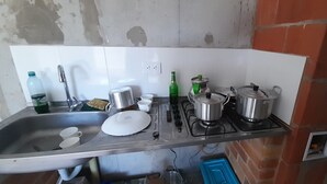 Een keuken met een spoelbak, kraan en fornuis. Op het aanrecht staan pannen, een fles en bekers.