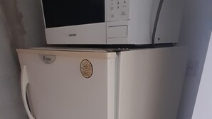 Een kleine, witte koelkast met een magnetron erboven, geplaatst in een hoek van een kamer met betegelde vloer.