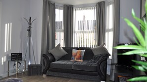 A modern living room with a grey sofa, a standing lamp, and a television. - VIP Church Street Apartments (Craigavon)