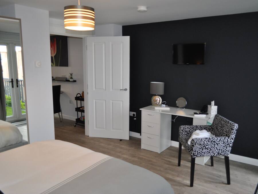 A bedroom with a bed, a desk, a chair, and a TV on the wall.
