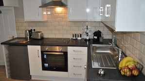 A modern kitchen with white cabinets, a stainless steel range hood, a built-in oven, and a sink. - VIP Church Street Apartments (Craigavon)
