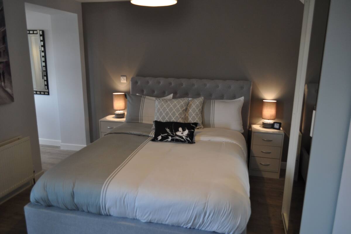 A neatly made bed with a tufted headboard, two bedside tables with lamps, and a nightstand with a clock.