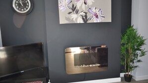 A room with a dark gray wall, a clock, a floral painting, a metallic object, and a potted plant. - VIP Church Street Apartments (Craigavon)
