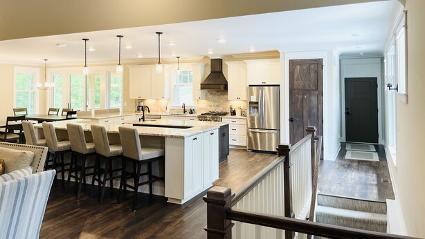 A spacious kitchen with a large island, white cabinetry, and a wooden staircase leading to another level.
