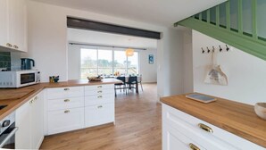 A modern kitchen with white cabinets and wooden countertops, a dining area with a table and chairs, and a view through large windows. - Avel Vaez - Charming house at 2 steps from the Aber Wrach (Landéda)
