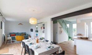 Een eetgedeelte met een tafel voor vier personen, een bank, een boekenkast en een trap die naar een andere kamer leidt.
