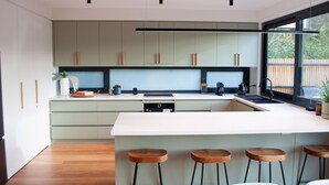 Een moderne keuken met lichtgroene kastjes, een wit aanrecht en een groot raam.