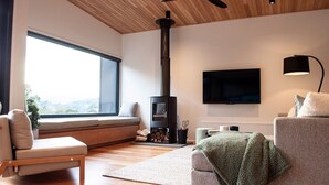 Een moderne woonkamer met een ingebouwde houtkachel, een groot raam, een flatscreen televisie en een gezellige zithoek.