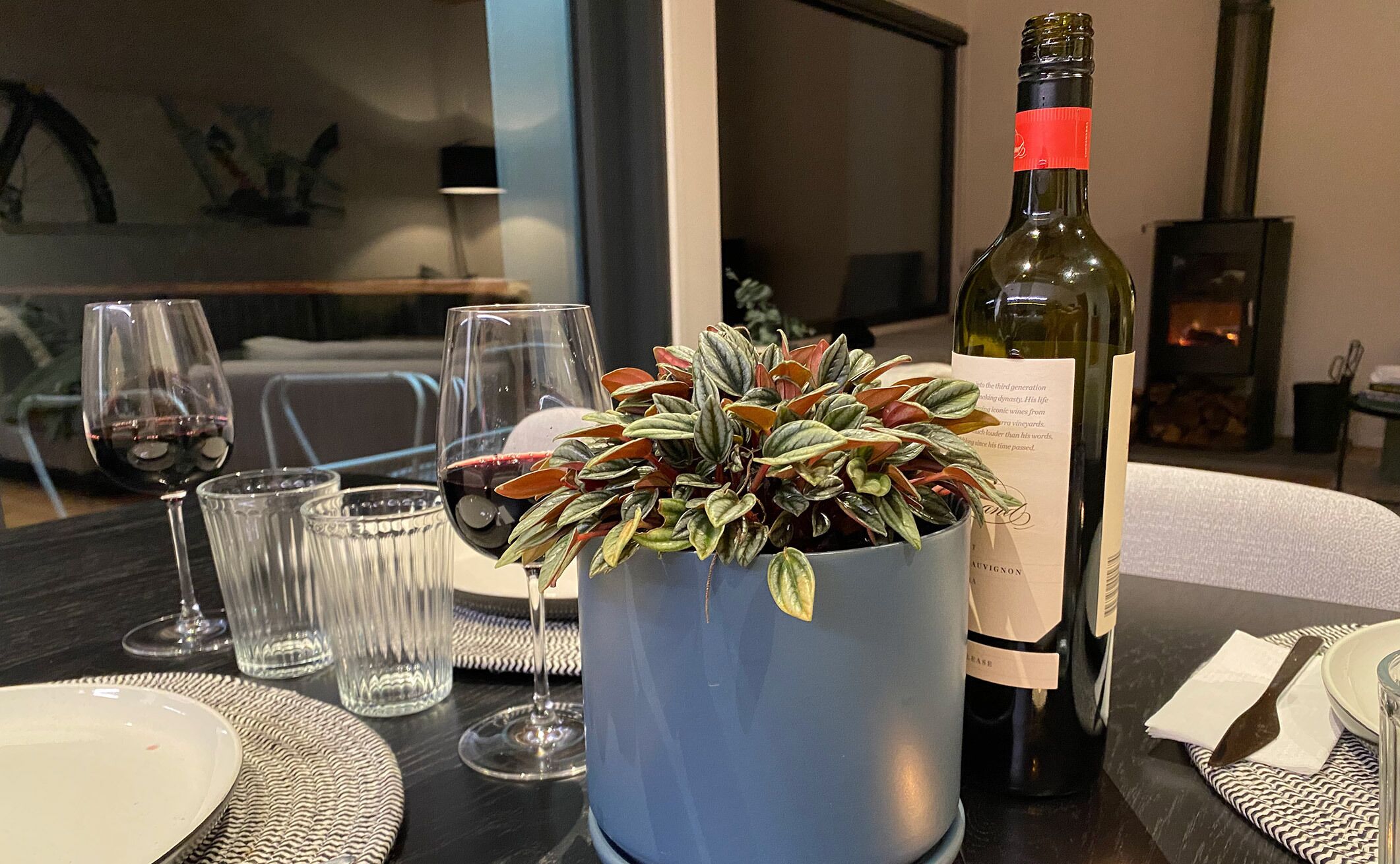 Een eettafel met een fles wijn, glazen en een potplant.