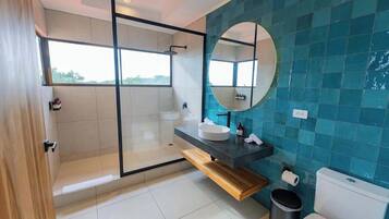 Une salle de bain moderne avec une douche à parois de verre, un miroir rond, un lavabo blanc et des toilettes.