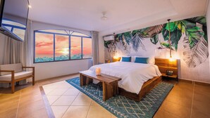 Un dormitorio con un ventanal grande, una cama, una mesita de noche, una silla y un mural en la pared.