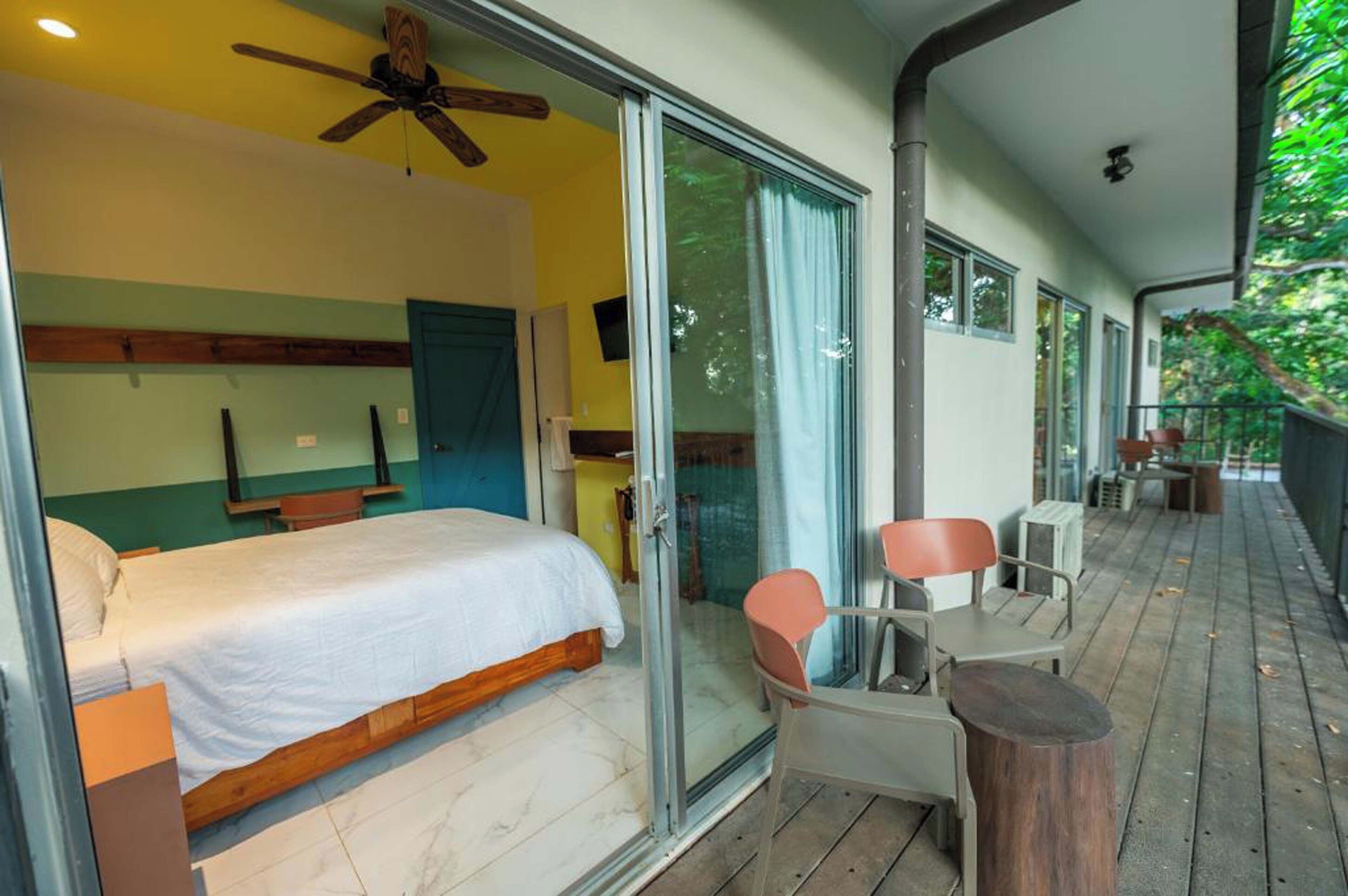 A bedroom with a bed, a ceiling fan, and a sliding glass door leading to a balcony with chairs and a table.