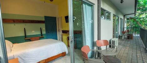 A bedroom with a bed, a ceiling fan, and a sliding glass door leading to a balcony with chairs and a table.