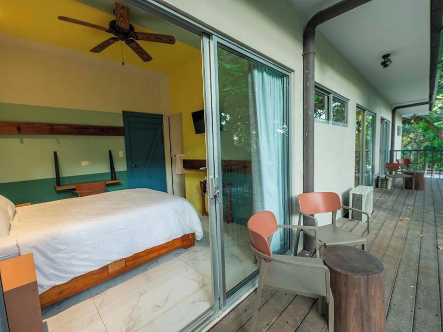 Un dormitorio con cama, ventilador de techo y puerta corrediza de vidrio que da a un balcón con sillas y mesa.