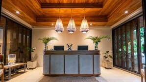 Un mostrador de recepción con detalles de madera, tres lámparas colgantes y plantas en macetas.