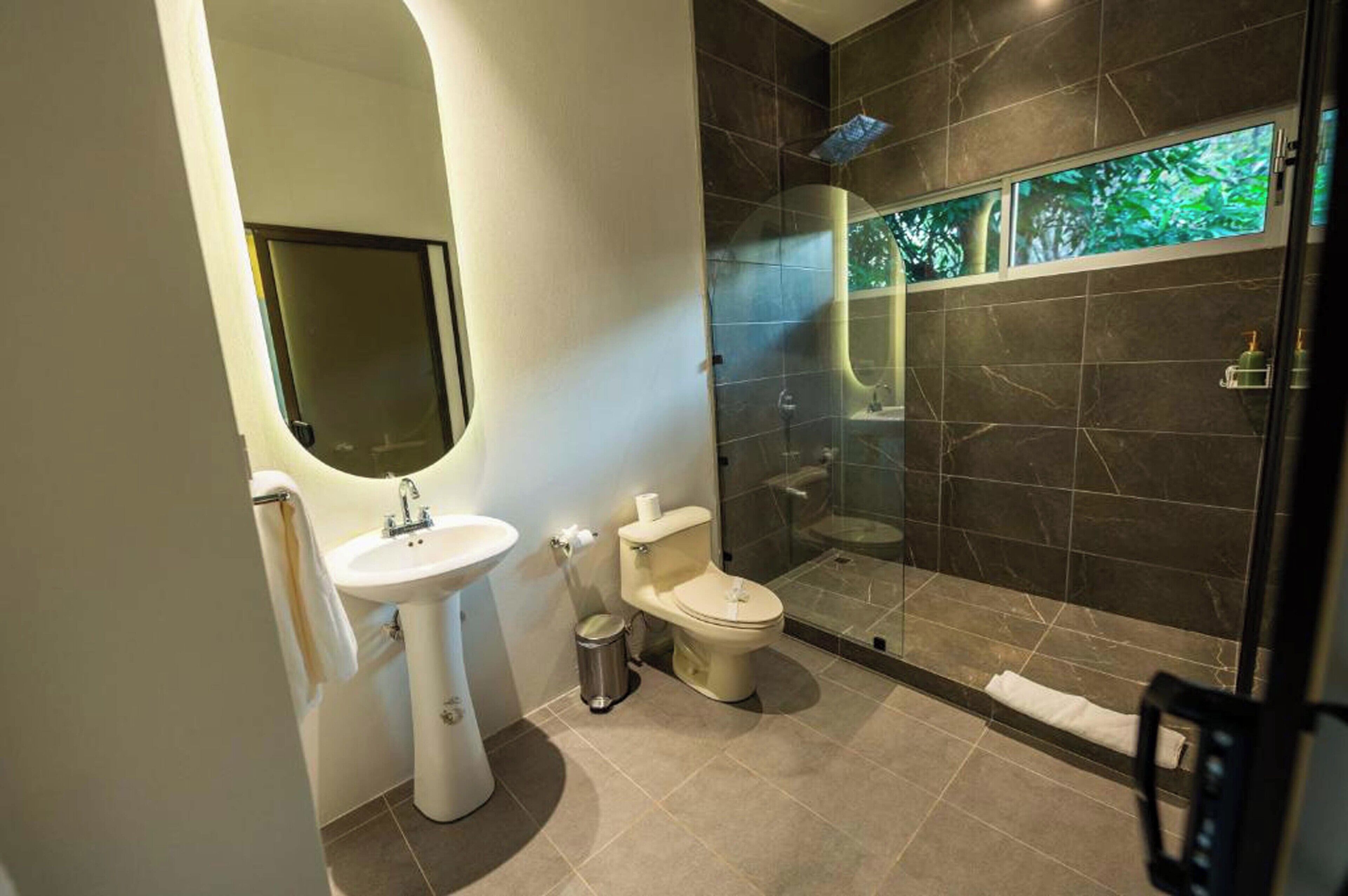 A modern bathroom with a pedestal sink, toilet, and glass-enclosed shower.