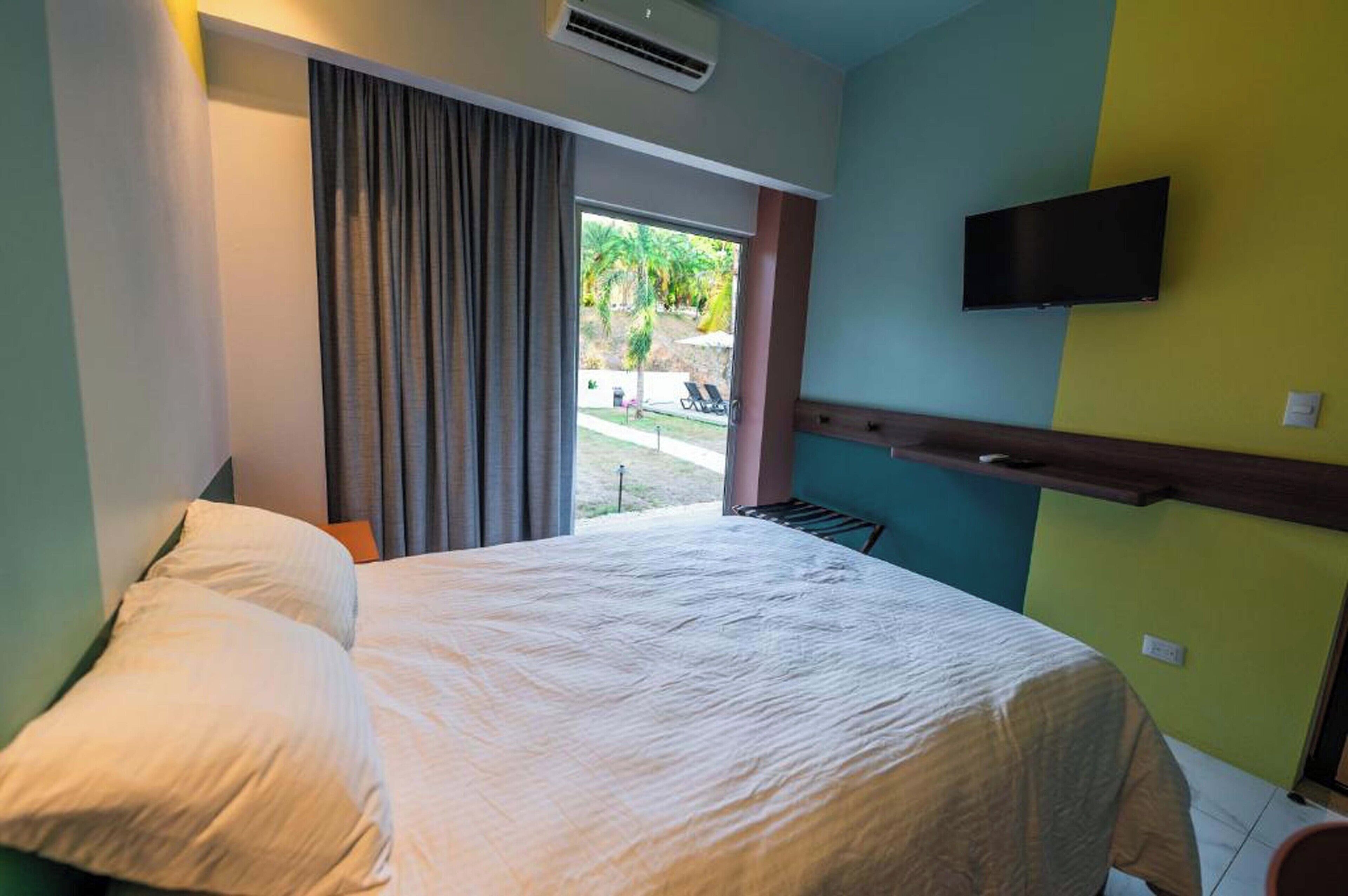 Habitación de hotel con cama, televisión montada en la pared y ventana con cortinas.