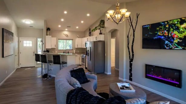 A modern living room with a sofa, ottoman, and a flat-screen TV mounted on the wall. - Prescott Perfection,  elegant 3 bedroom home (Prescott)