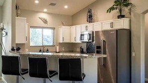 A modern kitchen with white cabinets, stainless steel appliances, a granite countertop, and black bar stools. - Prescott Perfection,  elegant 3 bedroom home (Prescott)