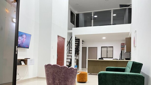 Un'ampia zona giorno con soffitto alto, una scala e un angolo cottura.