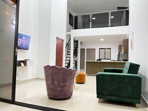 A spacious living area with a high ceiling, a staircase, and a kitchen area.