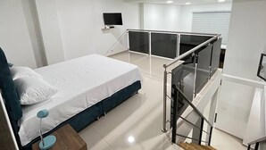 Camera da letto moderna con un letto, una scrivania, una televisione e un balcone con ringhiera in vetro.